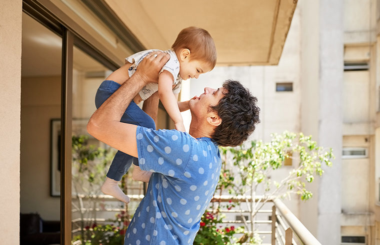 Father holding toddler boy over his head standing on apartment balcony - feature