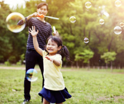 Asian girl chasing bubbles in the garden with father - feature