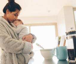 Sleepy mother holding baby in kitchen in morning- feature