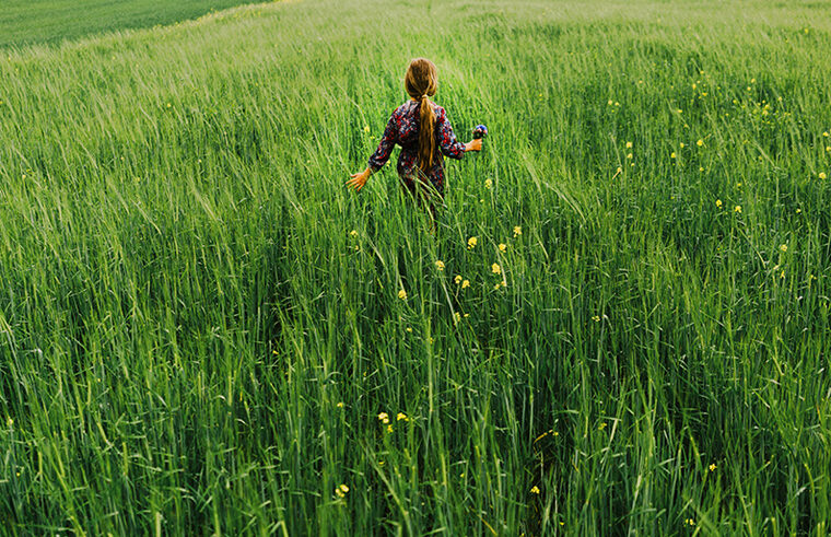 Girl walking through field of long grass with flowers