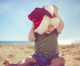 Toddler sitting on beach with Santa hat on - feature