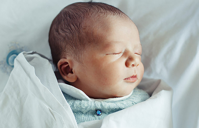 Newborn baby sleeping in blue jumper - feature