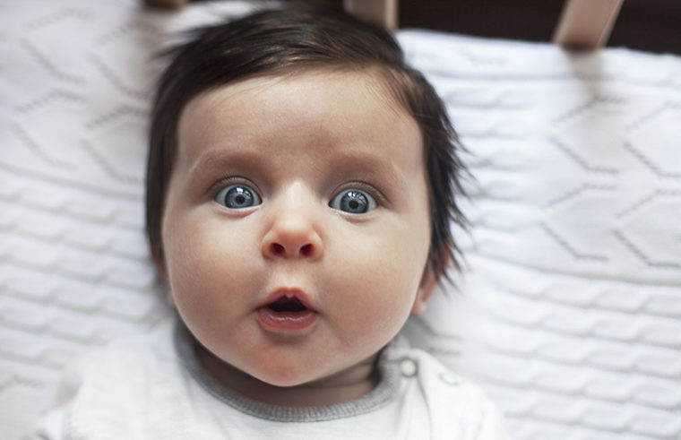 Surprised baby lying in cot - feature