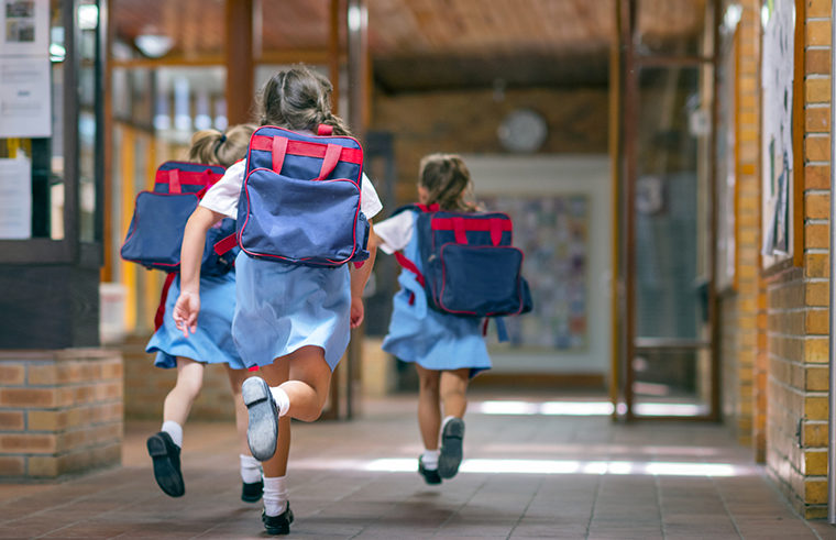 School girls with backpacks running in hallway - feature