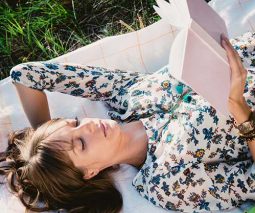 woman lying on rug in park reading book