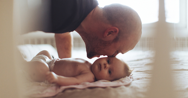 Father leaning down to kiss newborn baby 