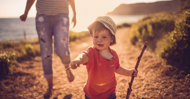 Toddler on beach with stick pointing