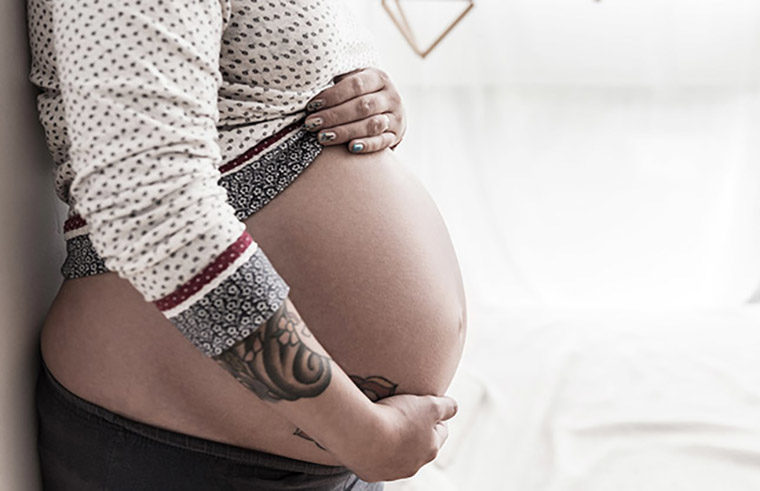Pregnant woman with arm tattoo holding belly - feature