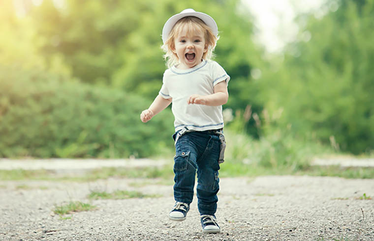 toddler boy in hat running on path