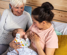 Mother breastfeeding newborn baby with grandmother looking - feature
