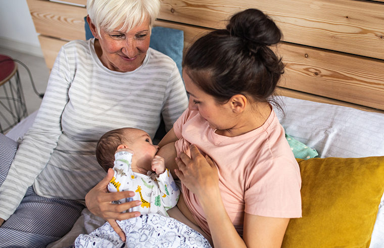 Mother breastfeeding newborn baby with grandmother looking - feature