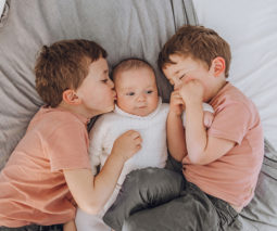 Two boys lying on bed with baby - feature