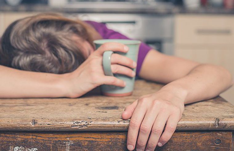 Woman holding coffee with head on table tired