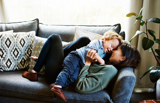 Mother lying on couch playing with toddler boy in her arms