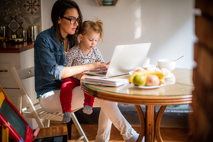 Young mother working from home with toddler girl on her lap