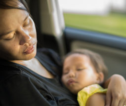 Tired mum asleep with baby in car