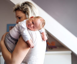 Mother holding newborn baby over shoulder - feature