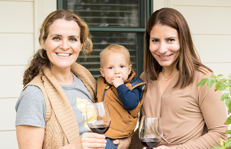 Mother holding baby drinking red wine with a friend