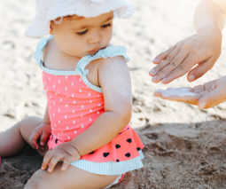 Baby on the beach with an adult applying suncream
