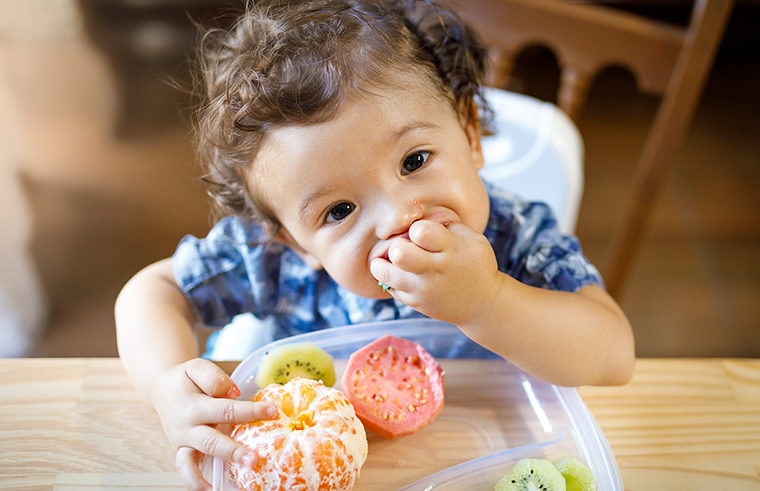 Toddler sitting at table with fruit feeding