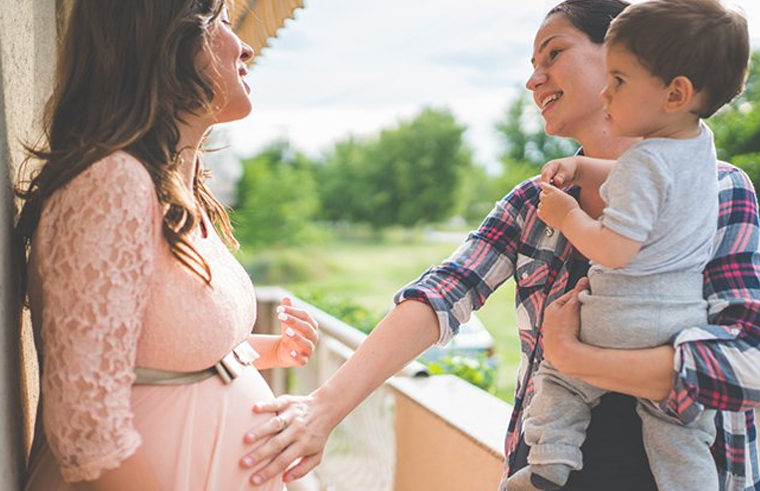 Woman holding toddler and touching friend's pregnant belly