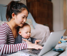 Asian mother with baby on lap looking at laptop computer - feature