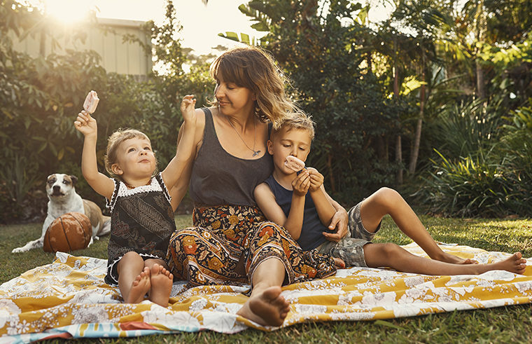 Mother and two children outdoors playing on rug - feature