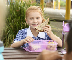 Girl in school uniform eating sandwich from lunch box - feature
