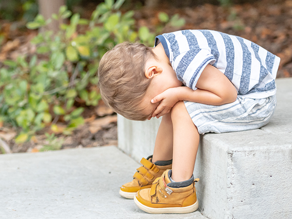 Sad toddler boy sitting on a step with head in hands