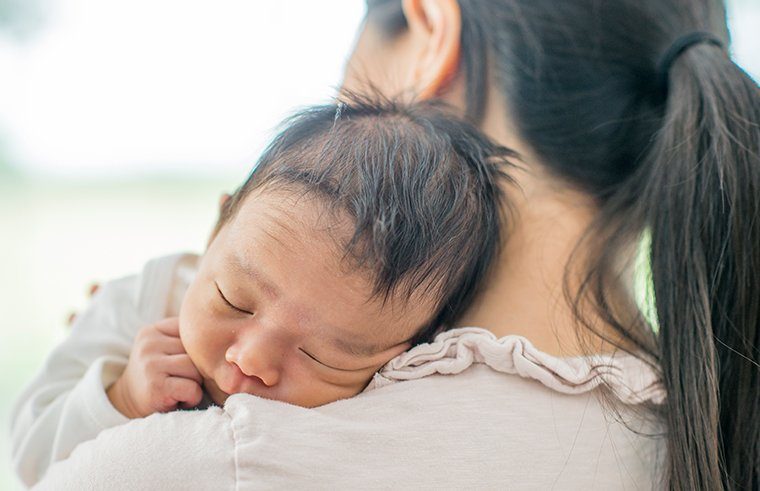 Asian baby asleep on mother's shoulder - feature