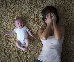 crying baby and mother with hands over her eyes