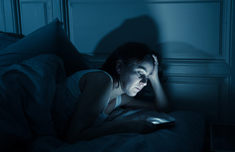 Anxious woman in bed looking at her phone feature