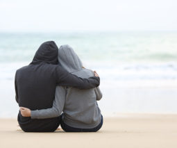 Sad couple sitting at beach in hoodies - feature