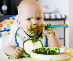 A baby eating something green and getting it all over him