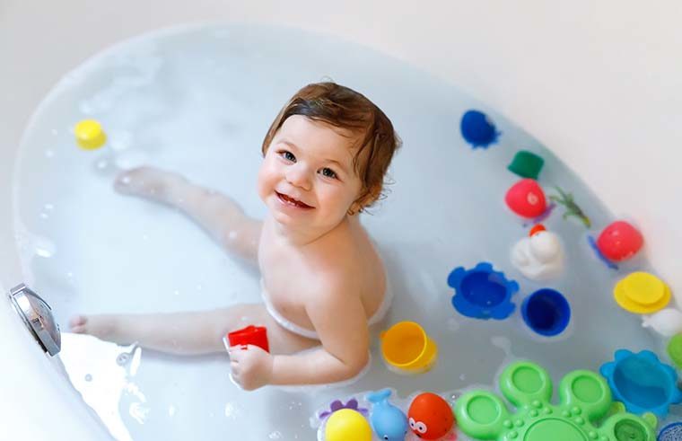 Toddler in bath with toys smiling - feature