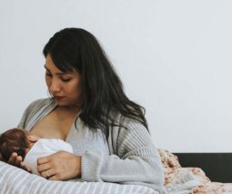 Mother sitting in bed breastfeeding newborn baby - feature