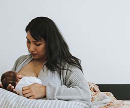 New mother breastfeeding newborn baby in bed - thumbnail
