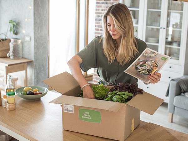 Woman opening box of fruit and vegetables delivered in kitchen