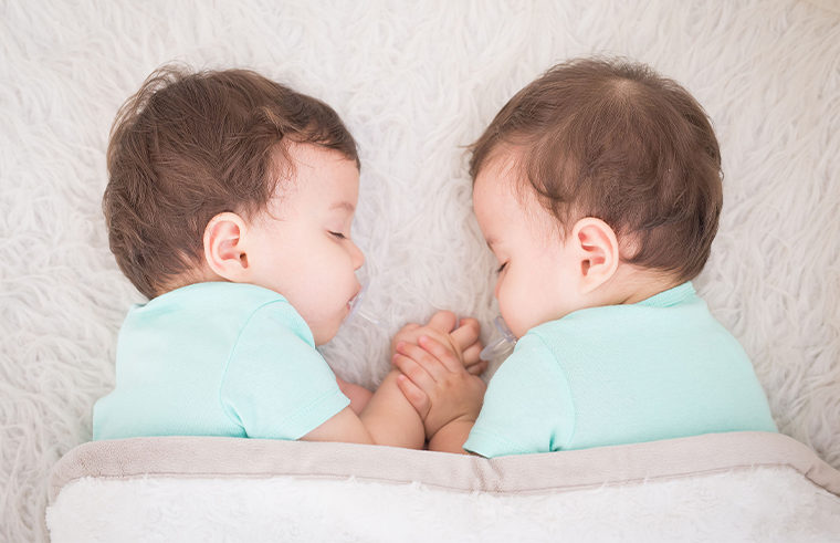Baby twins asleep holding hands with dummies in their mouths