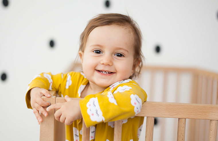 Toddler standing up smiling in cot