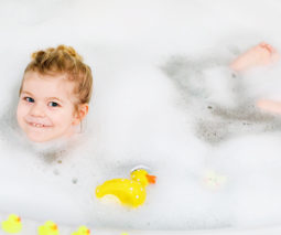 Toddler girl in bubble bath and toy ducks - feature