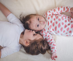 Baby and toddler sisters lying on bed overhead - feature