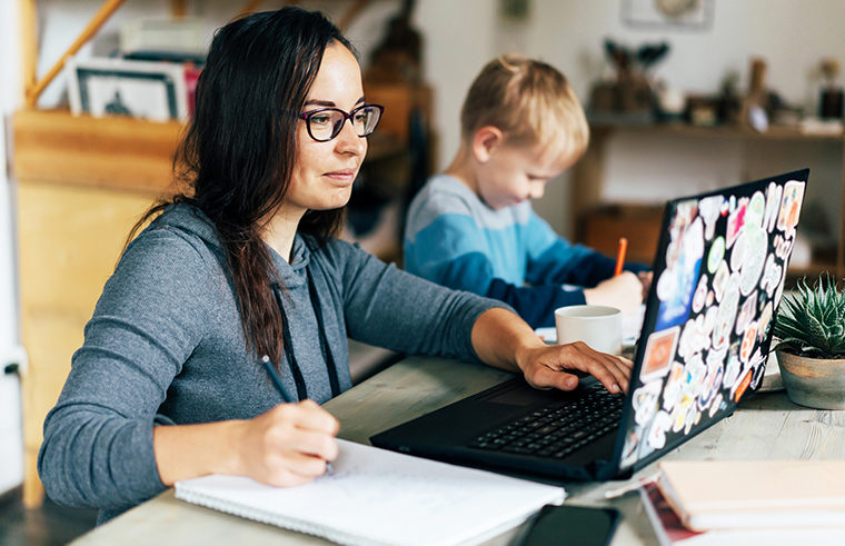 Mother working on laptop with young son working beside her - feature