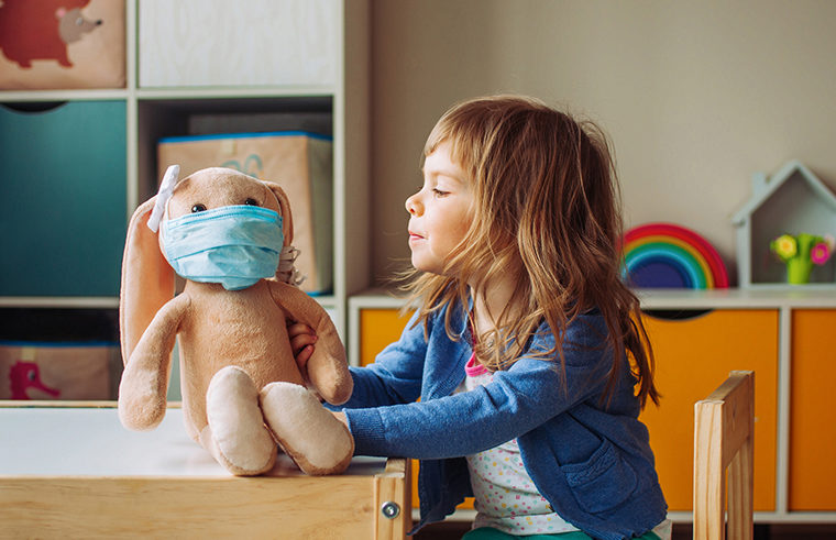 Young girl playing with a toy with a face mask on - feature