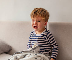 Toddler sitting on lounge with blanket crying