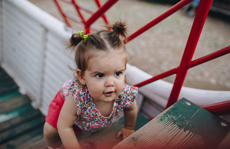Toddler girl climbing playground equipment - feature