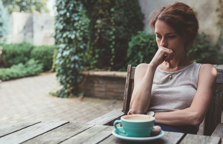 Woman drinking coffee outside alone - feature