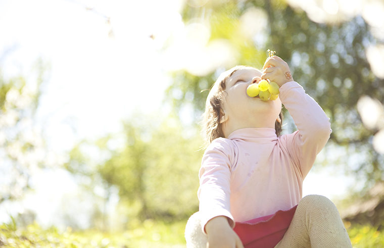 Toddler girl eating grapes outside