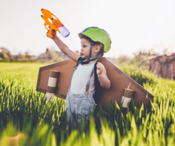 Boy standing in field wearing plane wings and holding a toy gun
