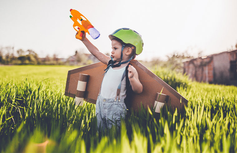 Boy standing in field wearing plane wings and holding a toy gun